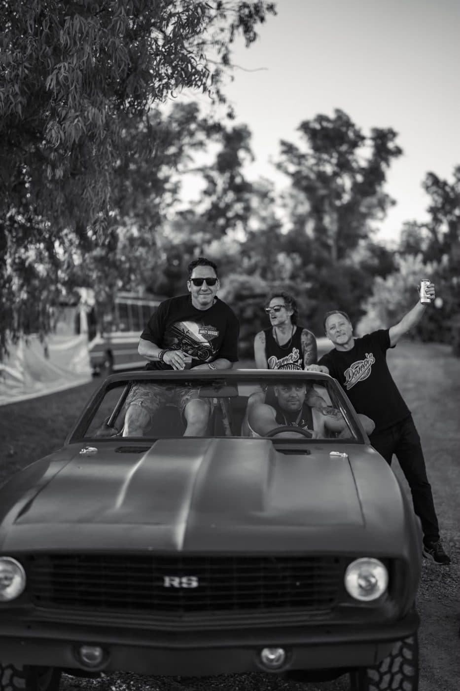 Tres amigos arriba de un Camaro RS, en blanco y negro