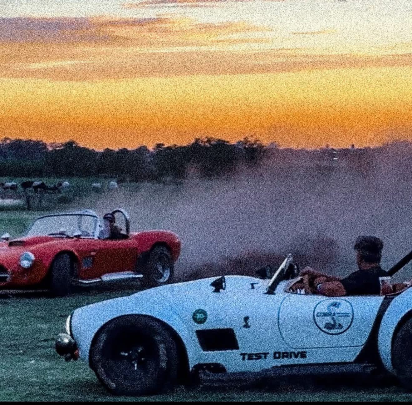 Dos Shelby Cobra quemando gomas con el cielo naranja del atardecer
